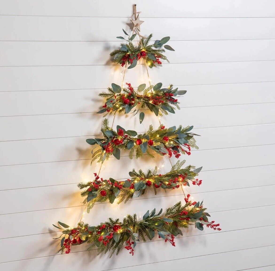 Lighted Hanging Wall Christmas Tree on a plain wall, showcasing its greenery, berries, and warm LED lights.