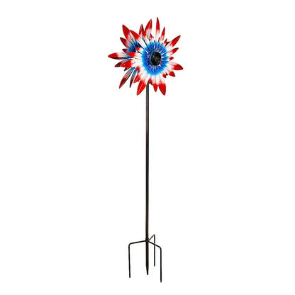 Patriotic wind spinner with red, white, and blue panels spinning in a garden setting. Image